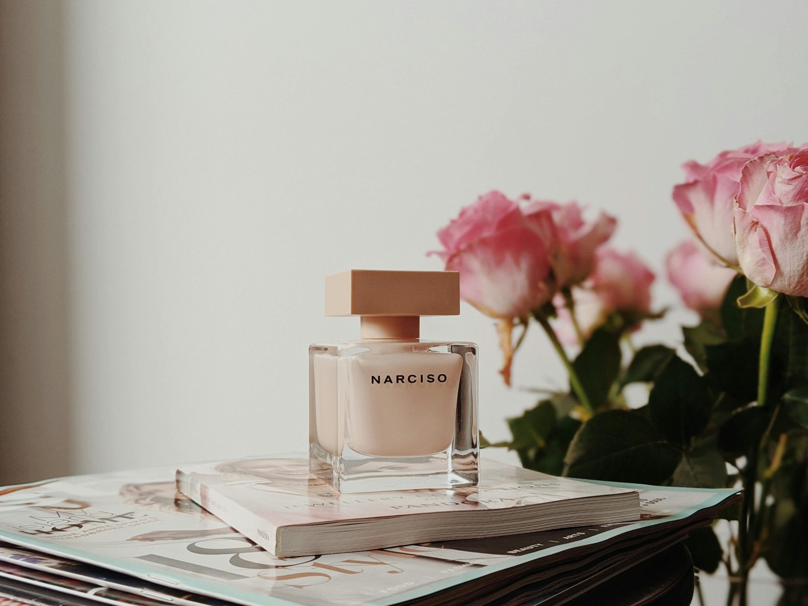 Sophisticated Narciso perfume bottle with pink roses and magazines. Perfect for elegance and fragrance themes.