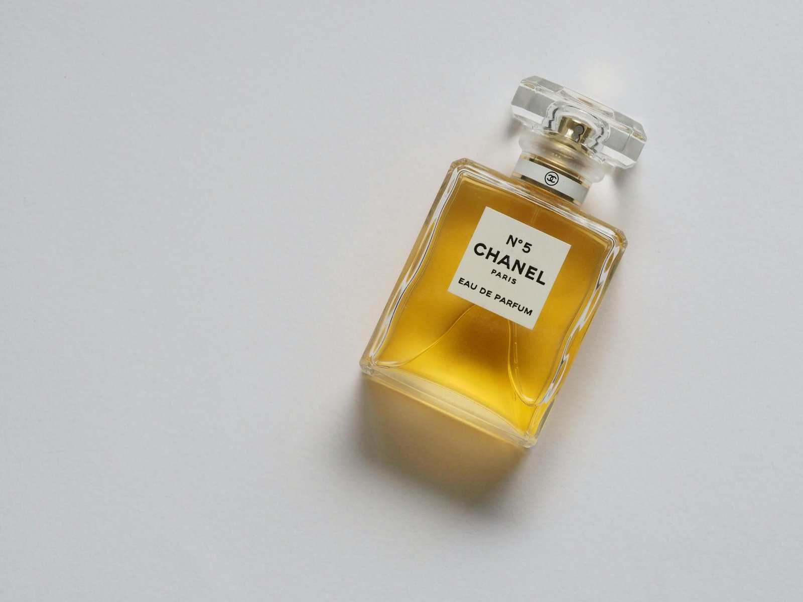 Elegant eau de parfum bottle with luxurious golden liquid on a minimalistic white background.