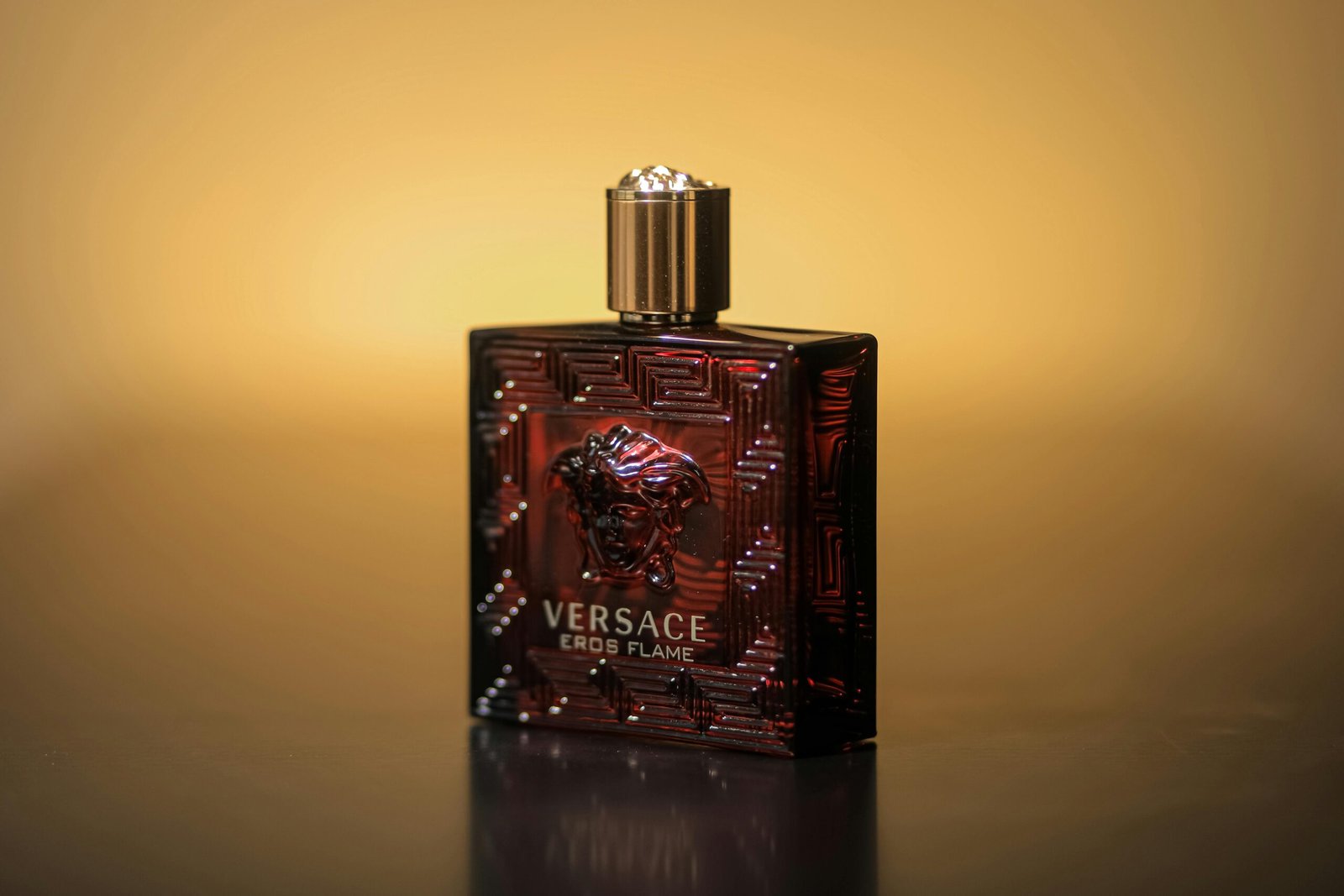 Close-up of Versace Eros Flame perfume bottle with a warm yellow backdrop.